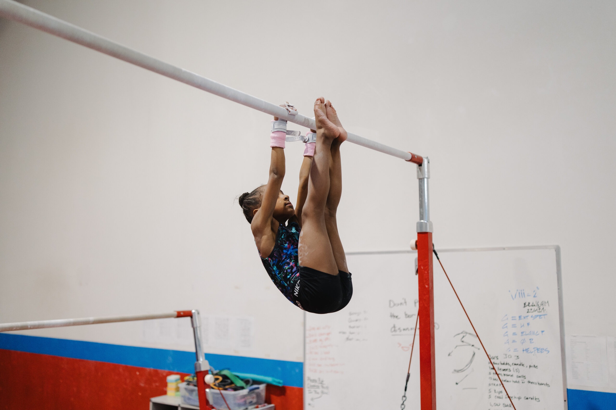 A young gymnast performing a leg lift while hanging from a high bar to build core and upper body strength.