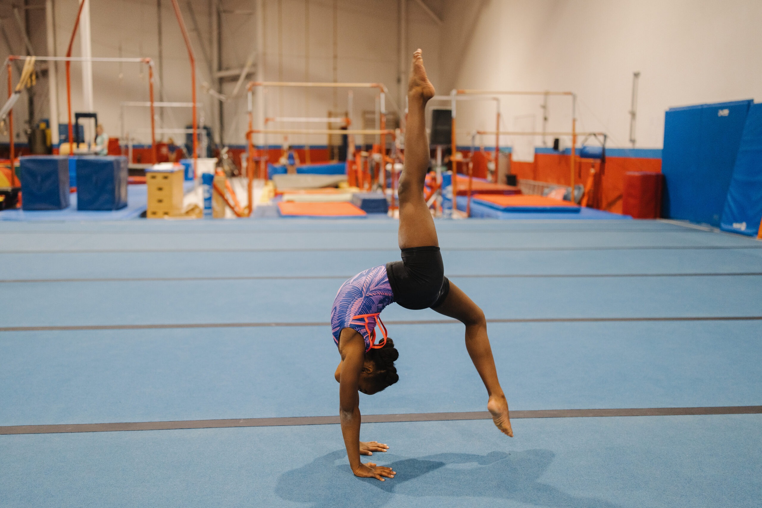 A gymnast in a red leotard performing a back handspring on a blue floor mat for the All Star Tumbling Program introduction section.