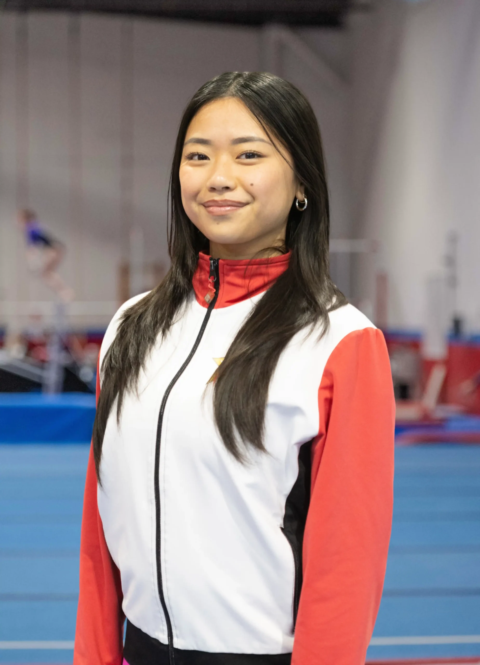 A professional headshot of Coach Abi wearing a red, white, and black team jacket.