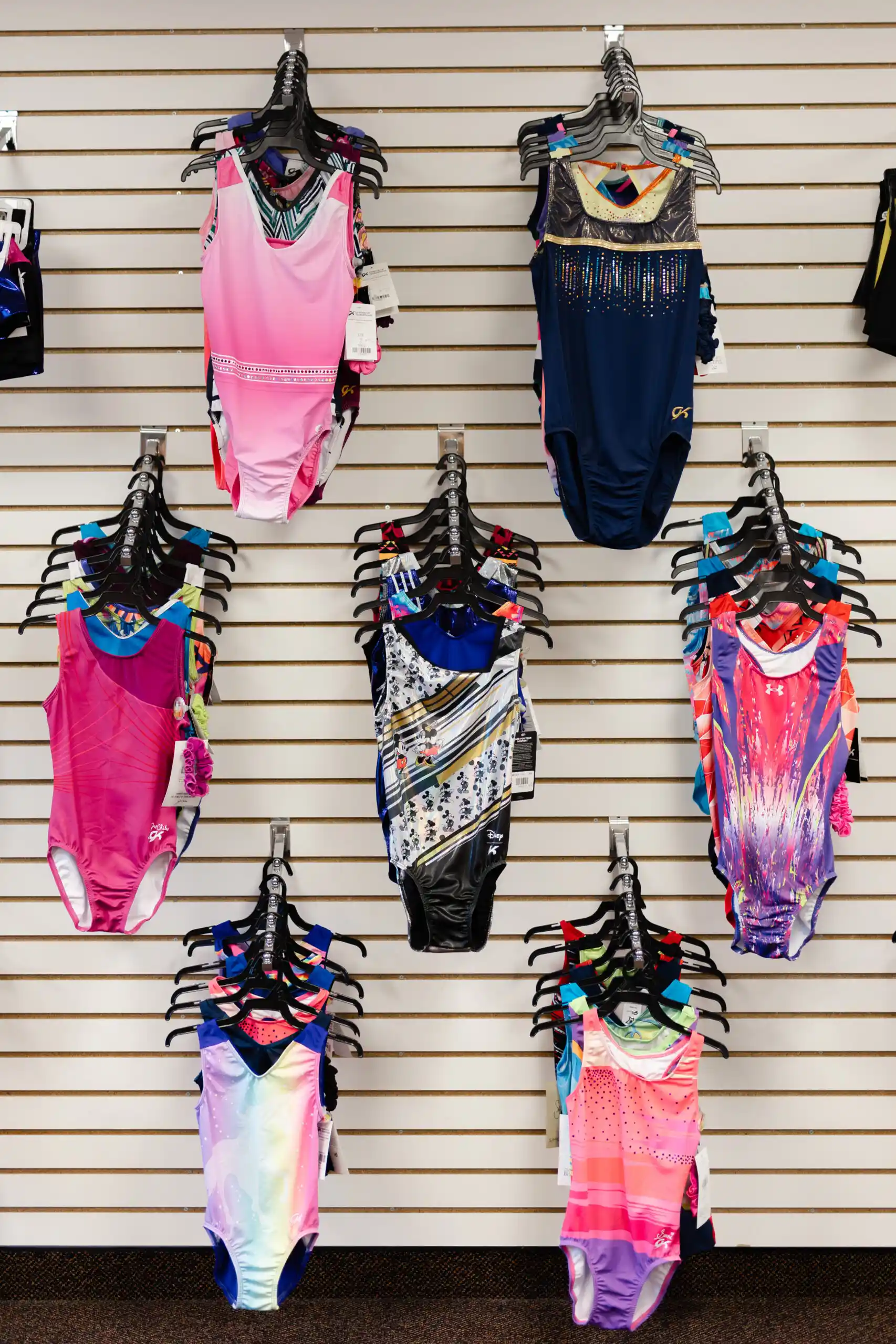 Colorful patterned gymnastics leotards hanging on a retail display wall.