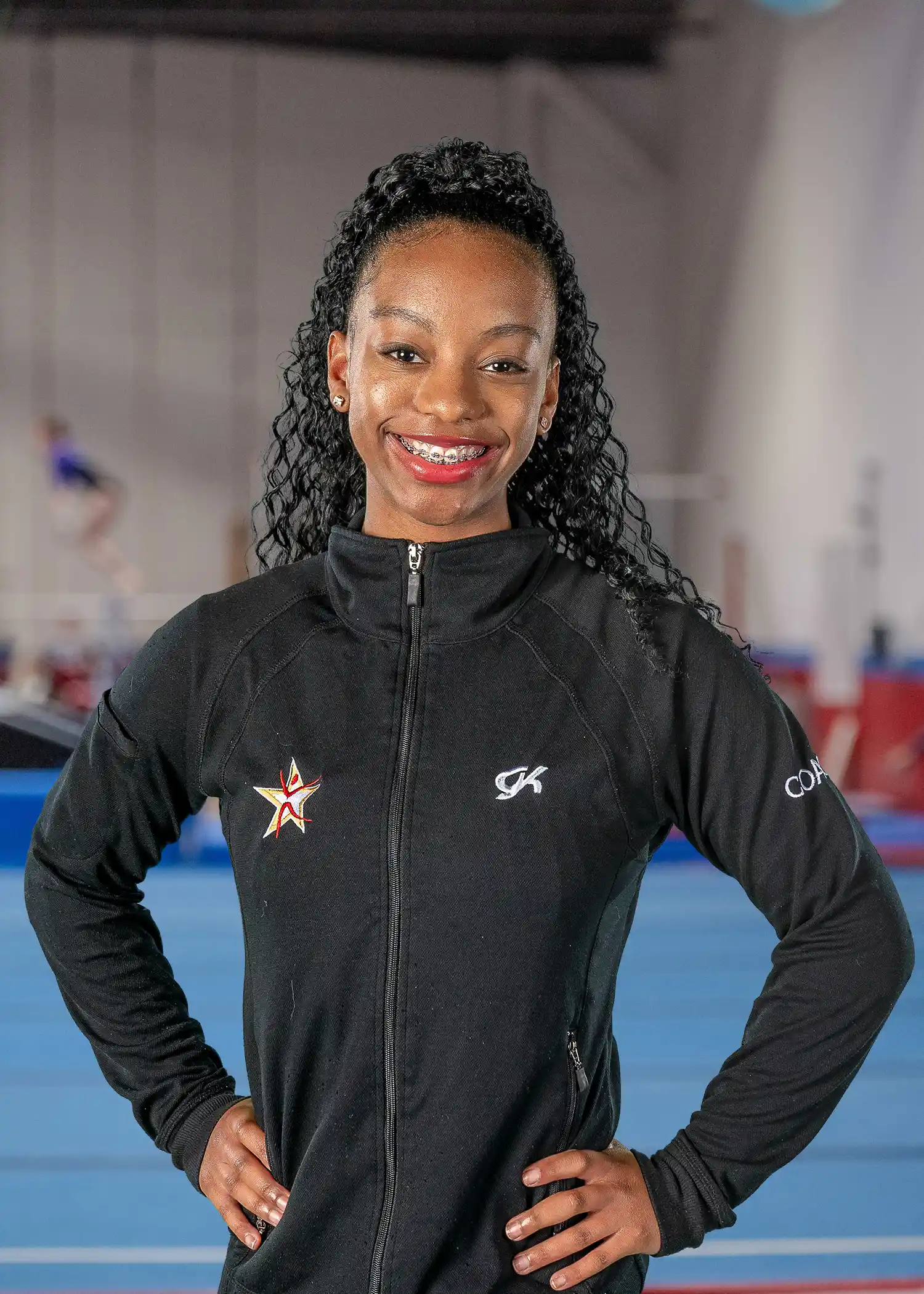 A professional headshot of Coach Giselle wearing a black team zip-up.