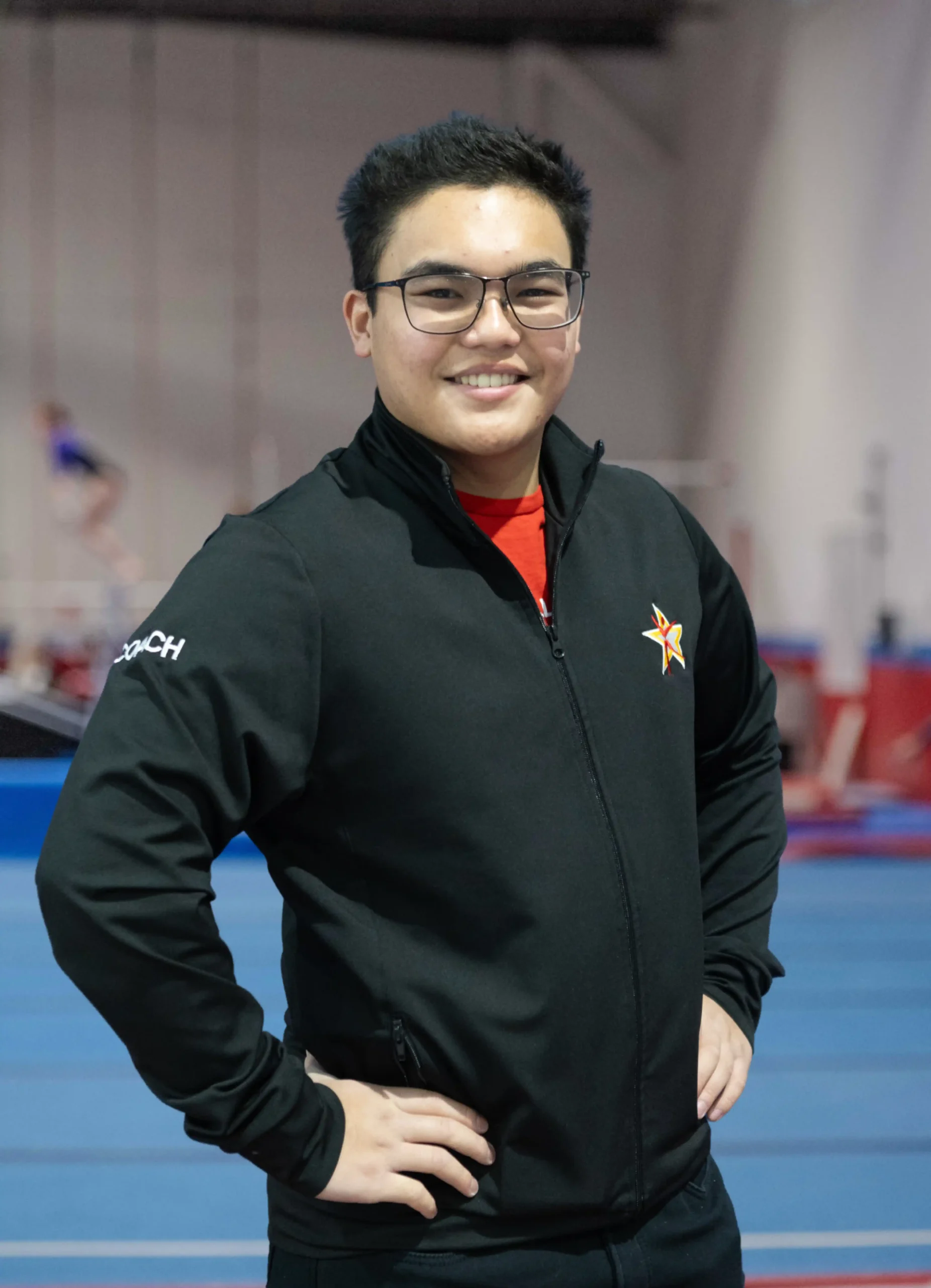 A professional headshot of Coach John smiling in a black team zip-up.