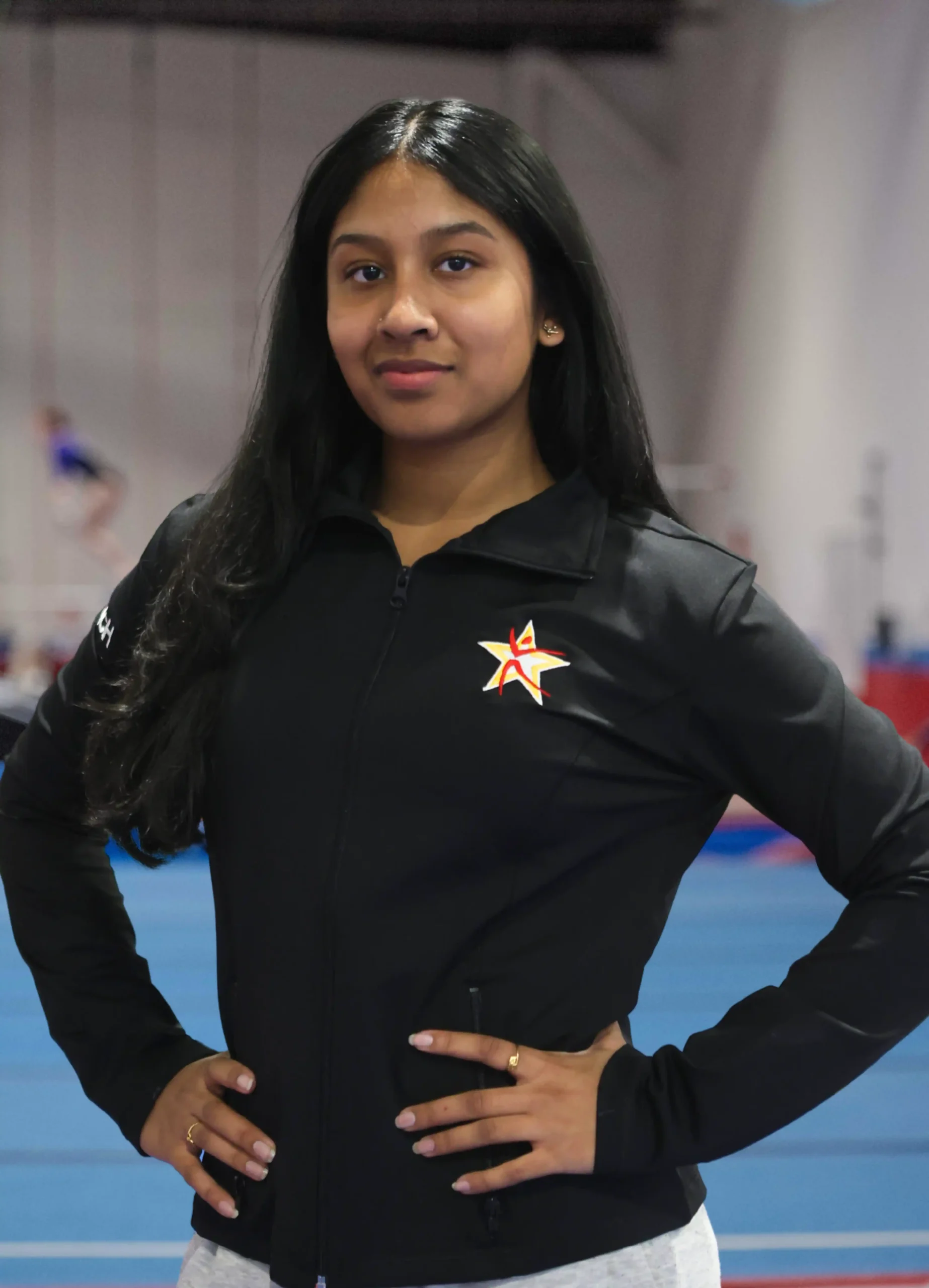 A professional headshot of Coach Karishma in a black team zip-up.
