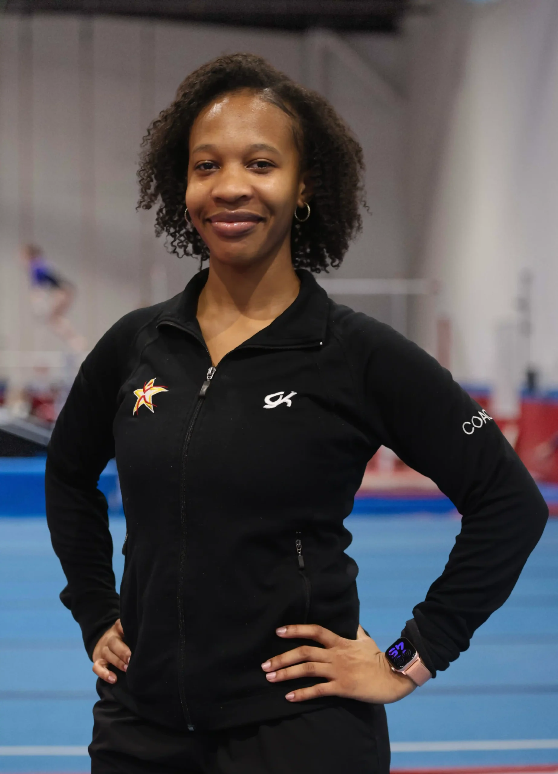A professional headshot of Coach Mikayla smiling in a black team jacket.