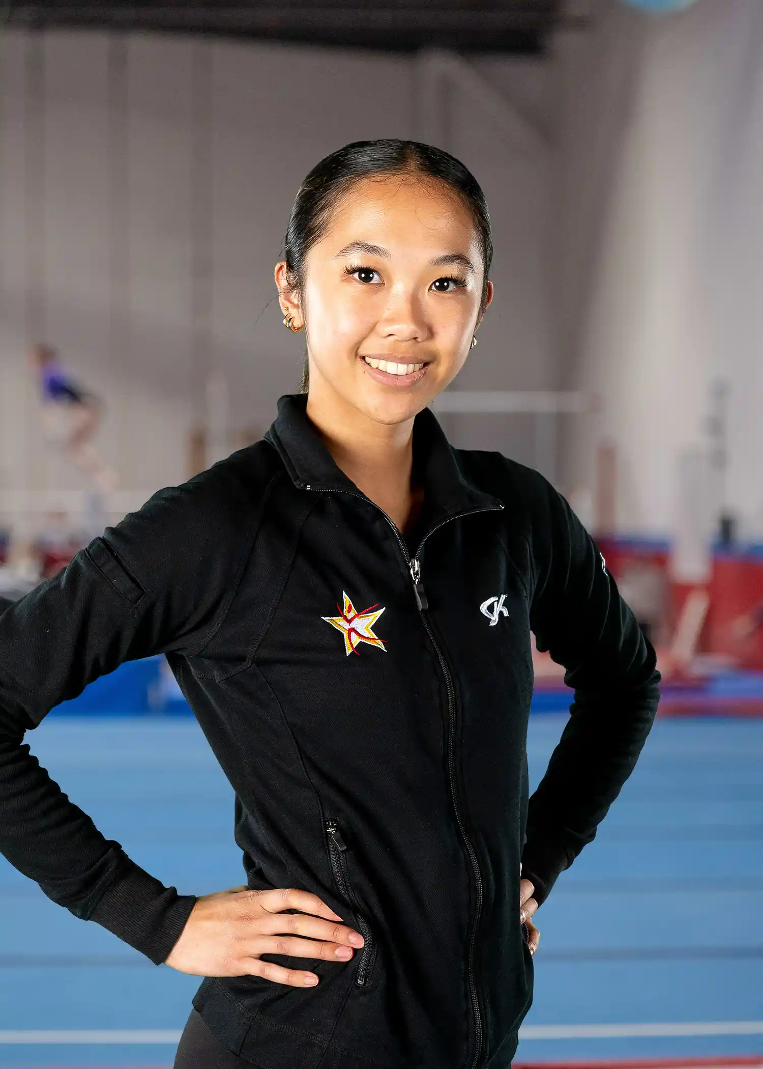 A professional headshot of Coach Raeniele posing in a black team zip-up jacket.