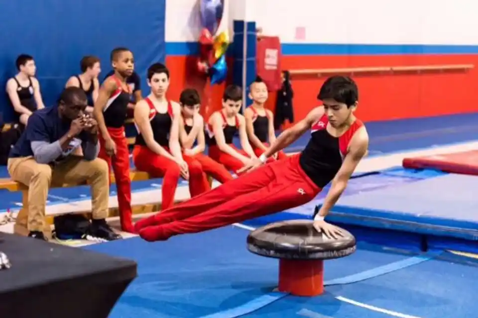 Young gymnast hanging from bars with focus. Text: "Focus. Strength. Grit. Goals. Developing Skills for Life."