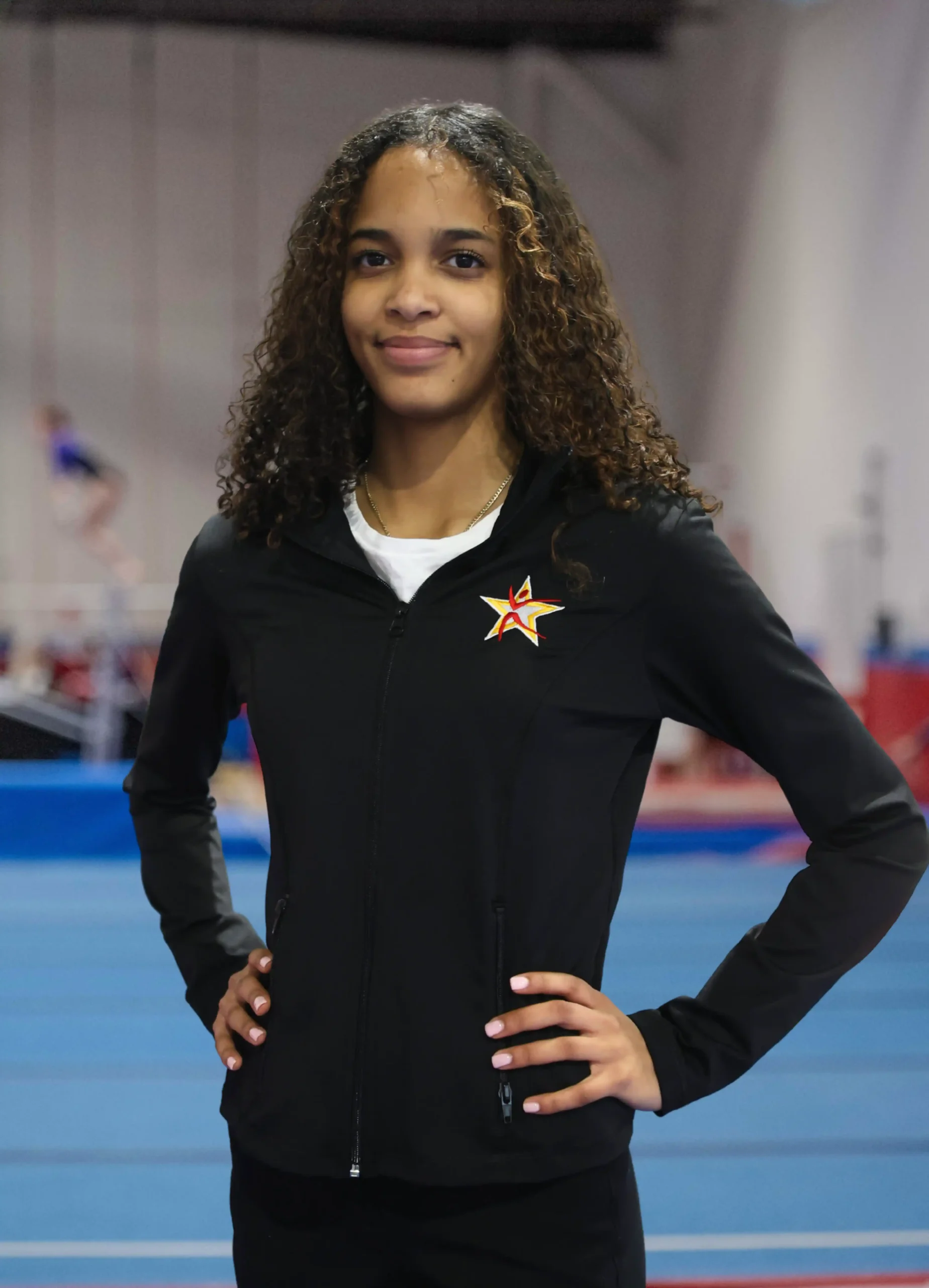 A professional headshot of Coach Zoraya posing in a black team jacket.