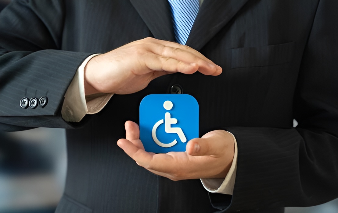 A person in a business suit holding their hands protectively around a blue accessibility icon featuring a person in a wheelchair.