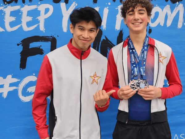 Two teenage male gymnasts in professional team jackets smiling while holding multiple silver medals in front of a blue event banner, representing the highest level of provincial and national competition commitment.